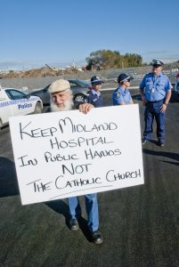Police remain on hand as a protestor displays a placard opposing the new campus.