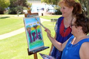 Professional artist and member of Identitywa, Wendy, oversees Adele during a painting lesson at Neil Hawkins Park in Joondalup. Photo: Supplied