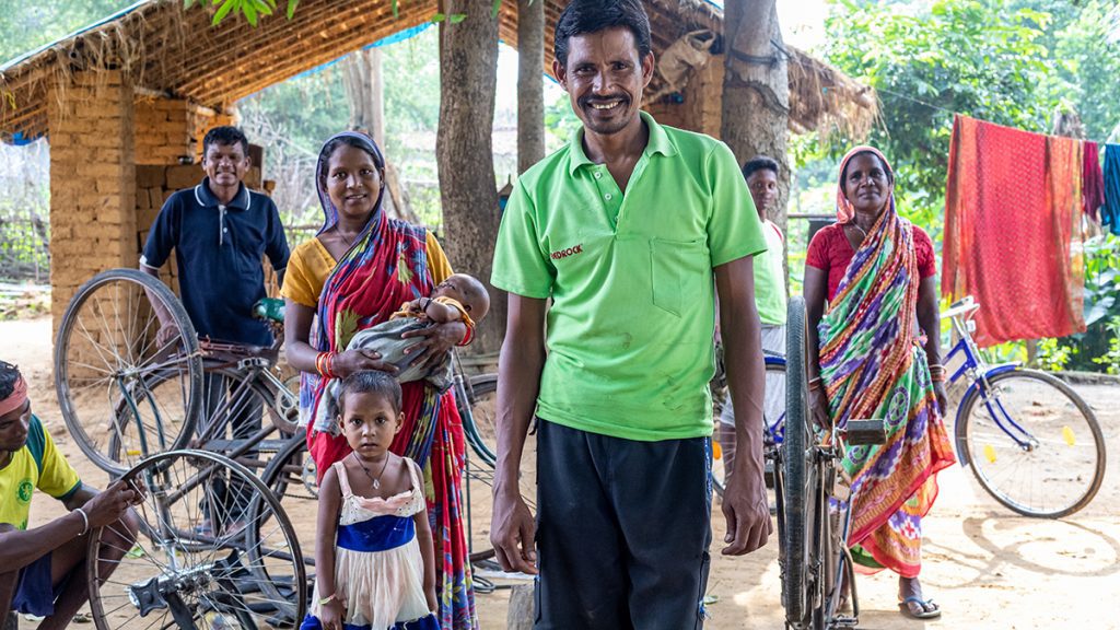 A man smiles at the camera with a group of villagers behind him.