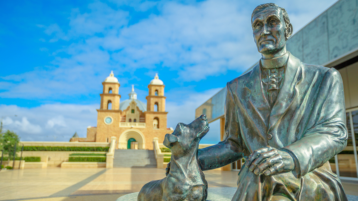 A statue of Monsignor John Hawes with one of his famous buildings, Geraldton's St. Francis Xavier Cathedral, in the background. Photo: Adobe.
